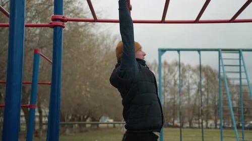 CloseUp of Coach Swinging on Red Iron Bar with Football Game in Background
