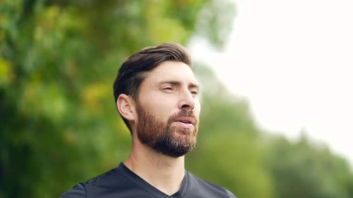 Close up portrait young happy bearded man standing in nature between forest trees relaxes, breathes