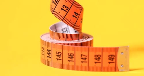 Coiled Orange Measuring Tape on Yellow Background