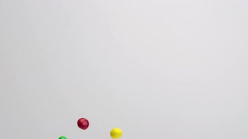 Bunte, mit Schokolade überzogene Erdnussbonbons, die in Zeitlupe auf weißem Hintergrund herabregnen