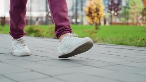 Leg View Walking Woman in Twenties Wearing White Sneakers and Burgundy Jogger Trousers