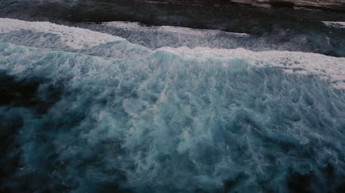 Aerial birds eye view of dramatic dark moody ocean water with white foaming waves breaking