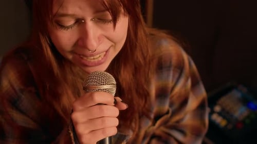 Redheaded Girl Singing into Microphone, Rehearsing in Dark Music Studio