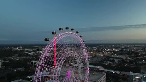 A vibrant cityscape at dusk featuring a glowing Ferris wheel with pink lights and a tall red observa