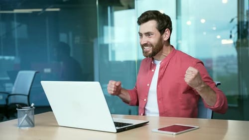 Man Celebrates Success at Laptop in Modern Office
