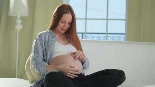 счастливая беременная женщина обнимает свой живот на диване