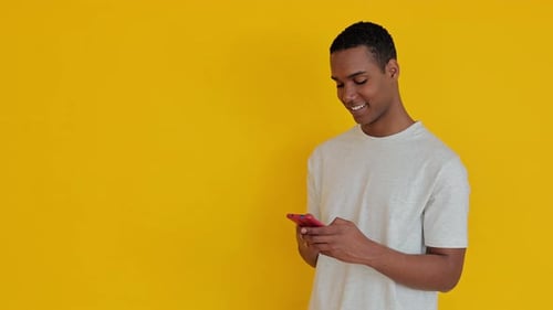 Young Man Using Smartphone Against Yellow Background