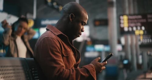 Focused Black Male Passenger Comparing Smartphone Data with Airport Information Board