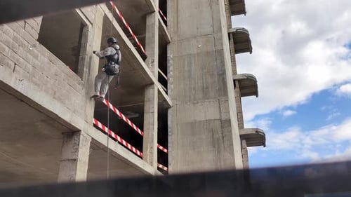 Unrecognizable Man in Gray Overall and Black Helmet Industrial Climber Ditches Wall of Concrete