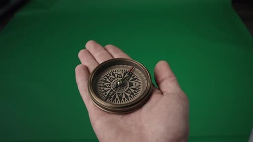 Travel Concept Magnetic Compass with a Rotating Arrow in an Open Male Palm on a Green Screen