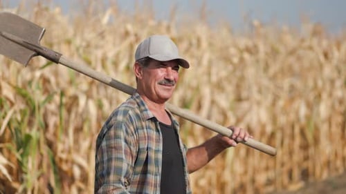 Senior Farmer with Shovel Posing on Country Road Beside Agricultural Land