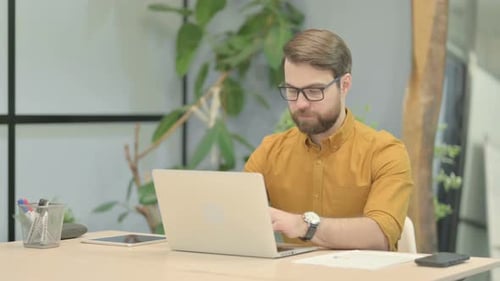 Young Man Smiling at Camera while using Laptop