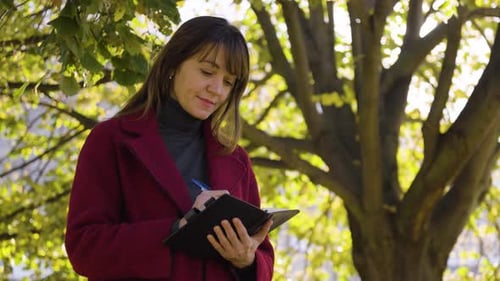 An Attractive Middleaged Caucasian Woman Writes Into a Notebook in a Park Ends in Closeup