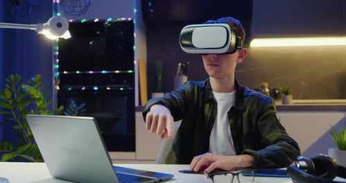 Teen Blond Caucasian Boy in VR Glasses Sitting in Evening Kitchen and Having VR Headset.