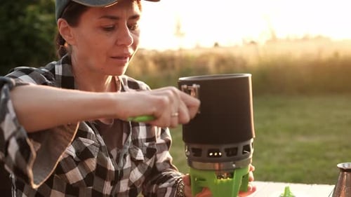 Woman Prepares Meal with Camping Stove at Sunset