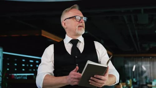 Confident adult businessman wearing white shirt and black vest with tie sands in the office.