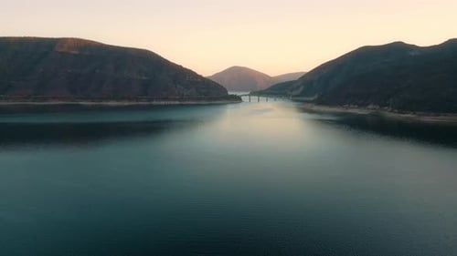 Aerial drone flying over a lake, water dam, with mountains at sunrise. Beautifull dreamy landscape
