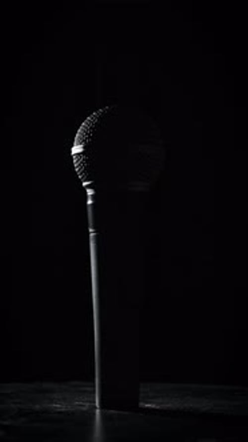 The Vocal Handheld Microphone Slowly Rotates in Backlight on Black Background