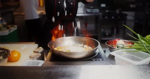 A woman in disposable black gloves, mixing the contents of a frying pan with fire, close-up