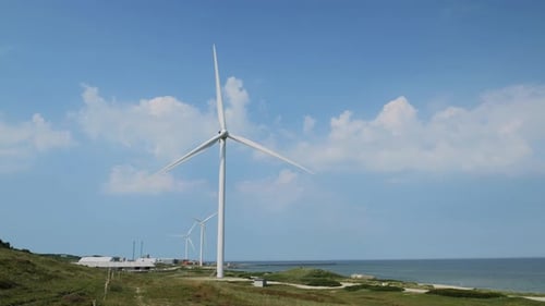 Wind turbine at the coast rotating slowly with sea and clouds in background.