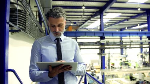 Ein Industriemann, Ingenieur, der in einer Fabrik steht und ein Tablet benutzt