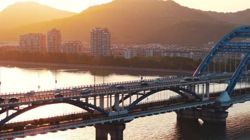 Aerial View of Numerous Cars Crossing a Beautiful Bridge As the Sun Sets Behind the Mountains and