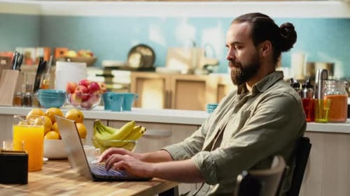 Man Using Laptop in Bright Kitchen Setting