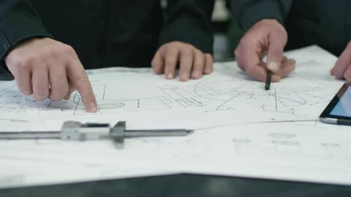 Close-up of two engineers discussing a blueprint in a factory.
