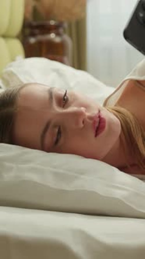 Woman relaxes in bed looking at phone