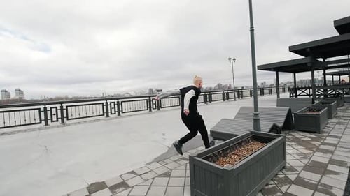 A Muscular Blonde Young Man Tracer Jumps Street Acrobatic Parkour