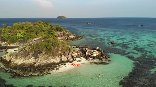 Aerial footage of a small island approaching a white shirtless man on top of rocks.