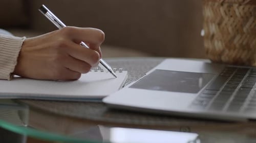 Writing in Notebook Beside Laptop on Glass Table
