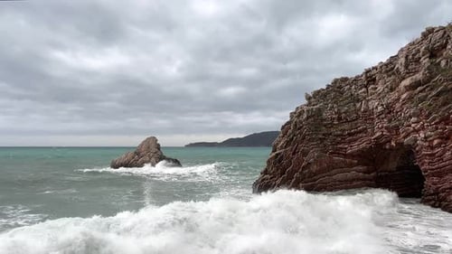 Large Foamy Sea Waves Crash on the Rocky Shore and Foamy Spray Flies Upward