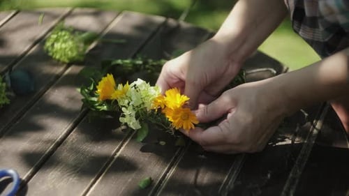 Hands Crafting Flower Wreath Outdoors on Wooden Table