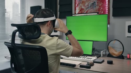 Person using virtual reality headset at desk with hand gesture and a green screen behind