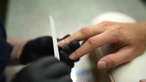 Nahaufnahme einer nicht wiederzuerkennenden Kosmetikerin in schwarzen Handschuhen, die die Nägel eines männlichen Kunden akribisch feilt