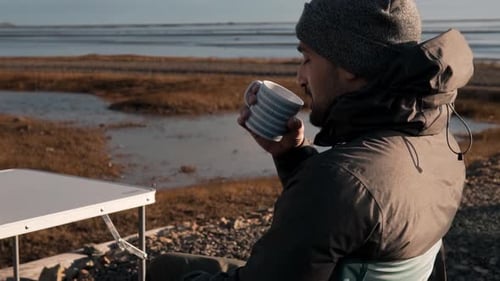 Man Drinking Coffee on Rocky Beach Shoreline