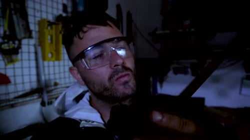 Man Inspecting Saw in Dimly Lit Workshop