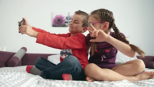 Children pose for smartphone selfie on bed indoors