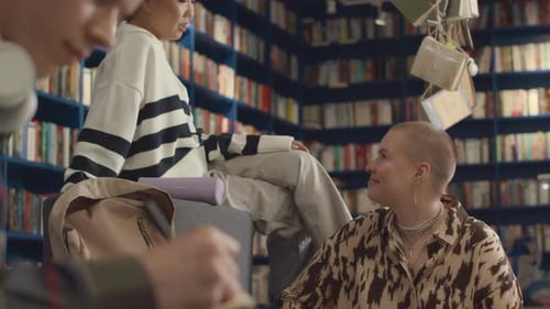 Two Cheerful Diverse Girlfriends Chatting in Public Library