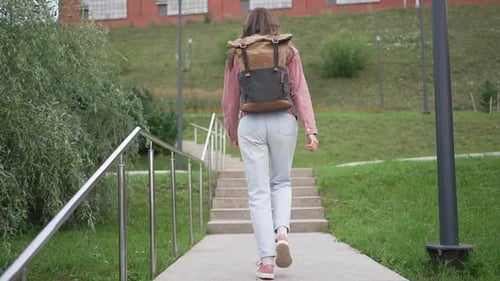 Young Woman in Casual Clothing and a Backpack Walks Up Concrete Stairs on a University Campus