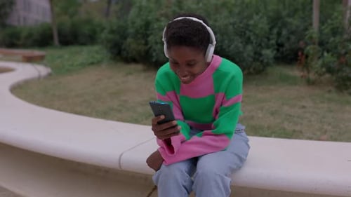 Young African Woman Using Mobile Phone Sitting Outdoors at City Street