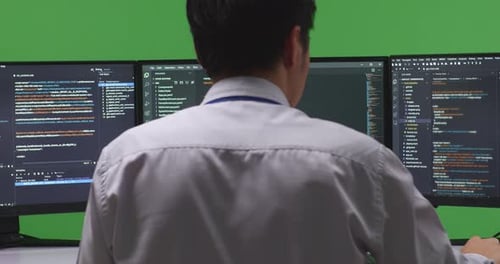 Back View Asian Man Developer Using Computer To Write Code With Multiple Screens In Green Screen