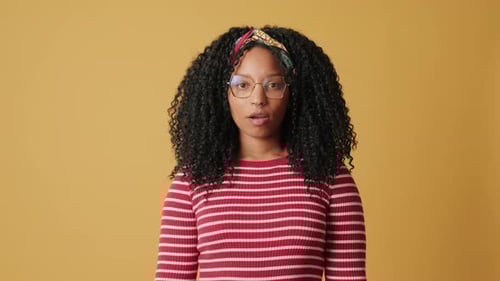 A young woman looks at the camera expressing dissatisfaction, on yellow background in the studio