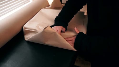 two men's hands pack the package in craft brown paper and place it in a brown paper box