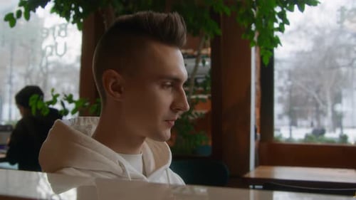 Young man alone drinks coffee in cafe. Stock footage. Handsome young man is drinking coffee alone.
