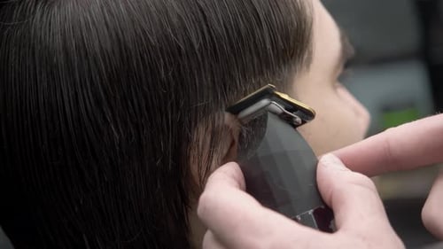 Ein Friseur verwendet einen Kamm und einen Trimmer, um die Haare eines jungen brünetten Mannes in einem Friseurladen ordentlich zu stylen