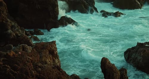 Ocean Waves Foaming on Dark Rocky Volcanic Shore in Twilight Raging Sea Turquoise Water Closeup