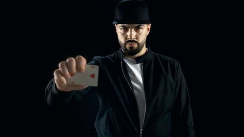 Professional Street Magician in a Cap Performs Impressive Sleight of Hand Card Trick. Background is