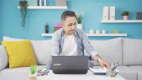 Man working on laptop throws files angrily.